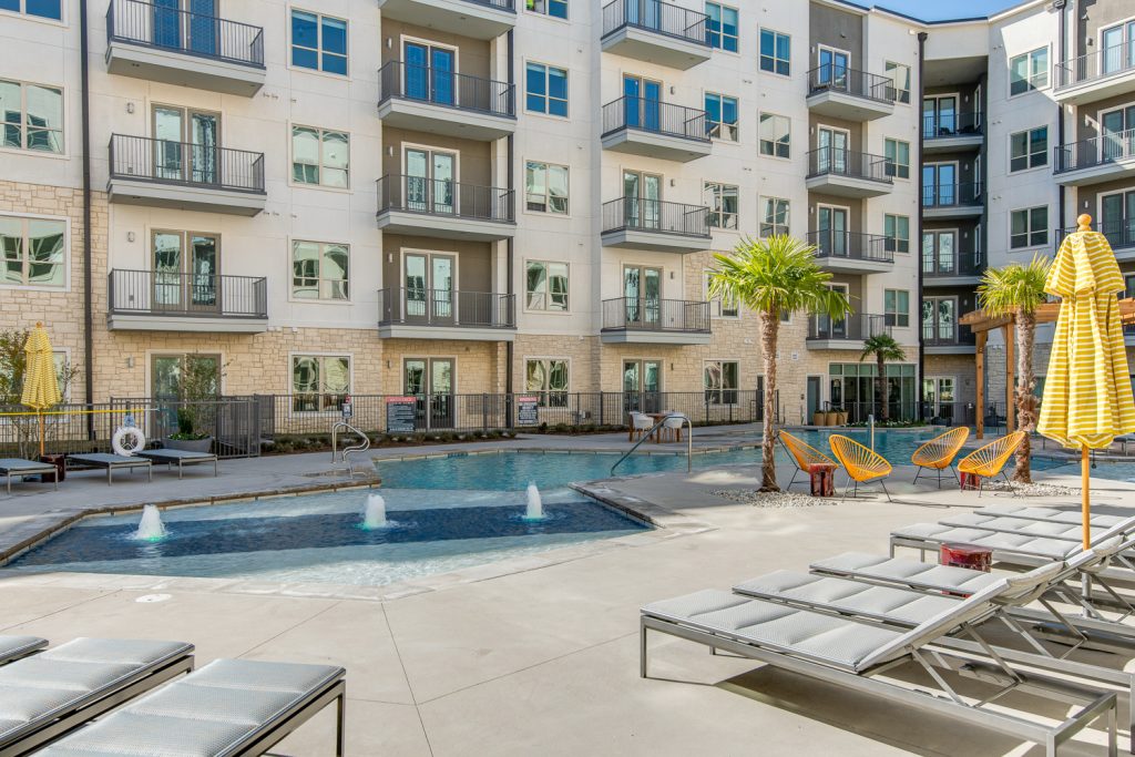 pool area with splash pad, lounge chairs, and palm trees