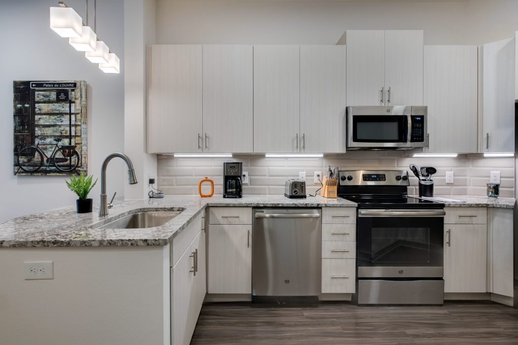 kitchen with granite countertops, overhead lighting, large sink, steel appliances, and wood flooring