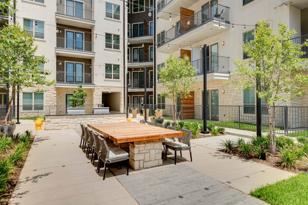 courtyhard area with large wooden table, seating, landscaping, string lights, and grills