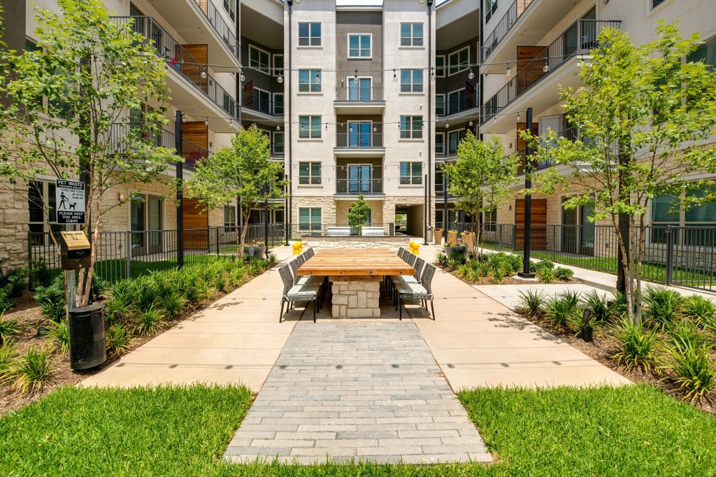 courtyhard area with large wooden table, seating, landscaping, and string lights