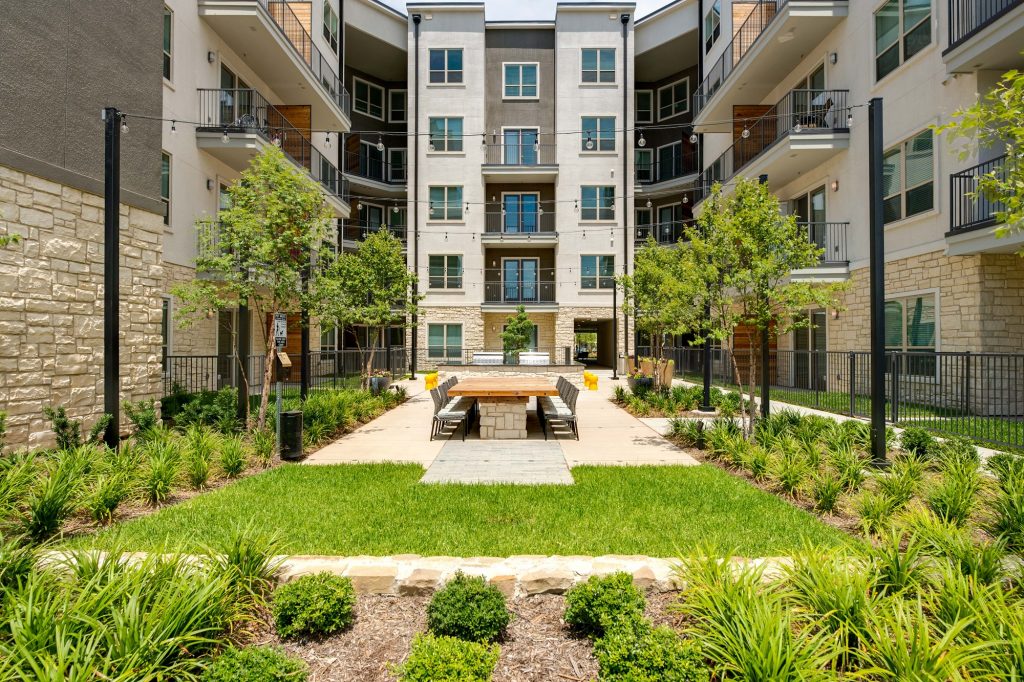 courtyhard area with large wooden table, seating, landscaping, and string lights