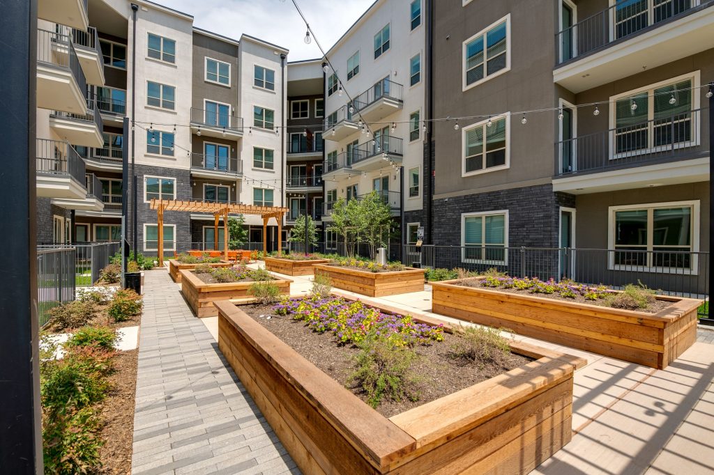 view from courtyard planters of outdoor area with large wooden table, seating, string lights, and wood pergola