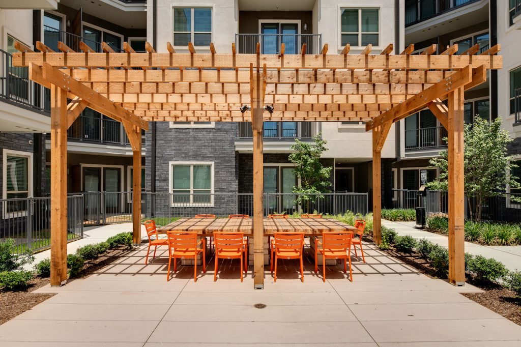 outdoor area with large wooden table, seating, and wood pergola with building view