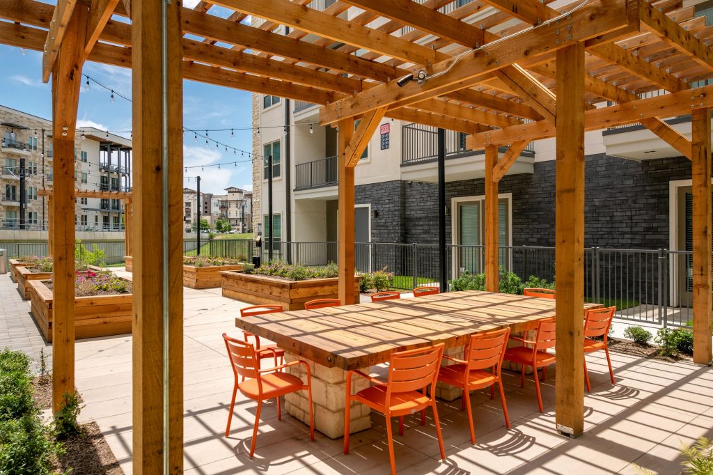 outdoor area with large wooden table, seating, and wood pergola and planters